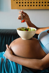 Detail of pregnant woman eating a healthy salad from a bowl on her belly.