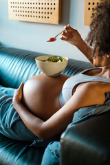 Relaxed pregnant woman eating a healthy salad from a bowl on her belly.