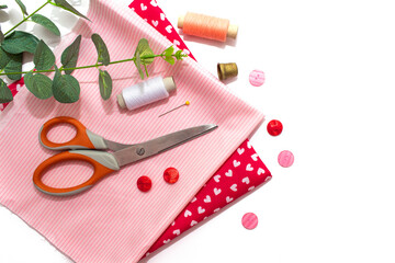 Sewing accessories, pink and red fabric on white background. Threads, needles, fabric, buttons and sewing centimeter.