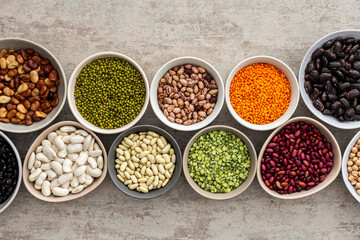 Different types of legumes in bowls, yellow peas and chickpeas , colored beans and lentils, mung beans, top view, copy space