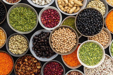 Different types of legumes in bowls, green with yellow peas and mung beans, chickpeas and peanuts, colored beans and lentils, top view