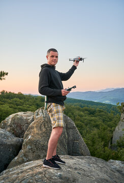 Man operating drone using remote controller. Man using drone at sunset for photos and video making while standing on top of high boulder in the mountains.