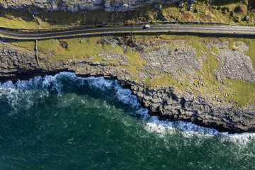 Top down view on a small road by a rough stone coastline. Rock formation and ocean water surface. Burren, Ireland