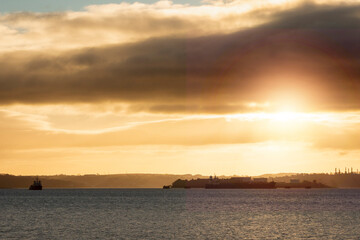 Early sunrise scene over ocean, Silhouette of a small island and a fishing boat. Warm orange color sky and sun flare. Tough live working on a boat.