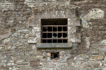 Prison window with metal bars and small ventilation for air. Old stone wall. Law correction facility for male and female offenders and criminals.
