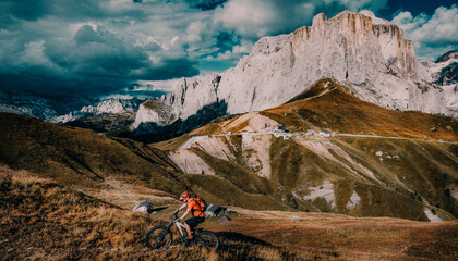 Uomo in bicicletta elettrica, percorre un sentiero di montagna nelle Dolomiti. Uomo che guida in bicicletta nel paesaggio di montagna. Pista ciclabile e-mtb enduro trail. Attività sportiva all'aperto. - obrazy, fototapety, plakaty