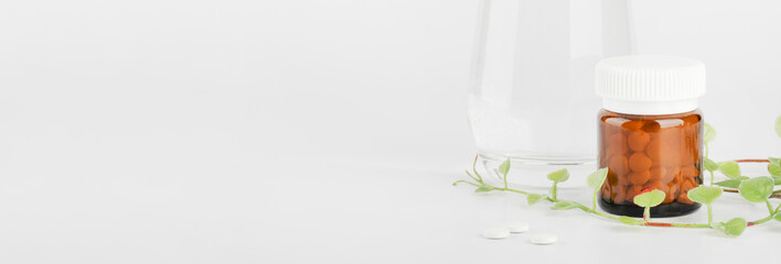 Herbal pills in glass bottle,green plant with glass of water on white background. alternative medicine and healthy lifestyle concept.copy space.banner