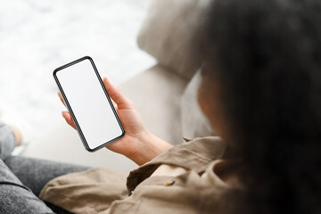 Cropped view of the young smiling woman sitting at the sofa at home and using smartphone, received unexpected good news. Technologies and people concept