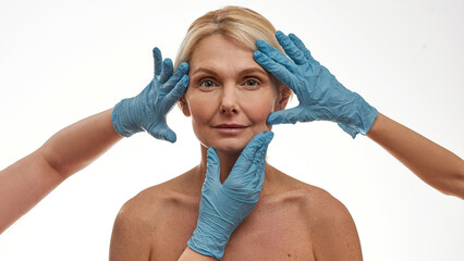 Plastic surgeons hands touch face of mature woman