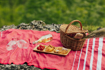 A summer picnic in a mountain with croissants, strawberry and a bottle of wine and two glasses. Beautiful rustic decor with basket with flowers. 