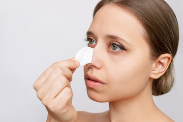 A young woman tears off the nose strip cleaning the skin of a face from blackheads or black dots isolated on white background. Acne problem, comedones. Enlarged pores on the face. Cosmetology concept