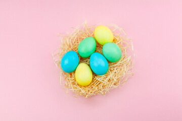Fototapeta na wymiar Easter eggs painted in pastel colors in hay nest against a pink background.
