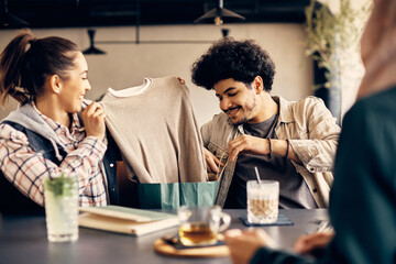 Happy Muslim man shows his female friends clothing he has bought in shopping.
