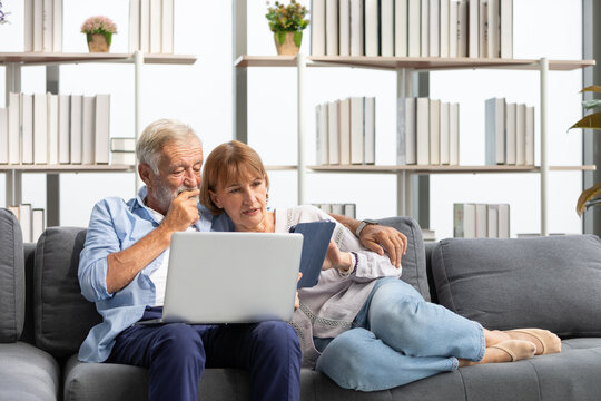 Senior Couple Using Laptop Computer And Tablet On Sofa