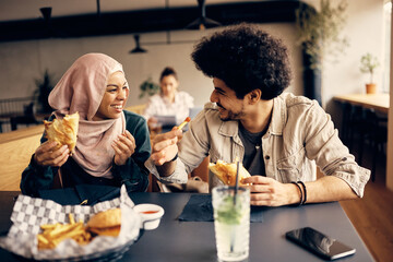 Cheerful Muslim woman and her male friend have fun while talking during lunch in cafeteria.