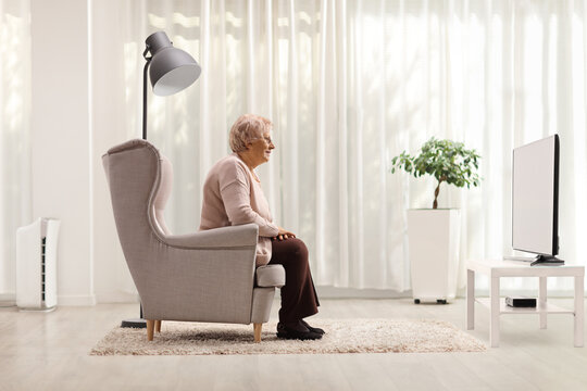 Elderly woman sitting in an armchair and watching tv at home - Powered by Adobe