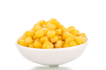 Bright yellow canned corn kernels in white ceramic saucer, macro, isolated on white background.