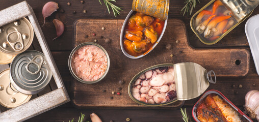 Various delicious canned fish and seafood in aluminum cans on the dark wooden background. Fast...