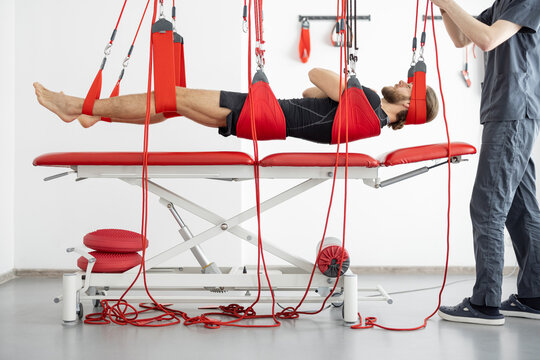 Male patient hanging on suspensions at rehabilitation center. Therapeutic exercises and neuromuscular activation on red cord slings