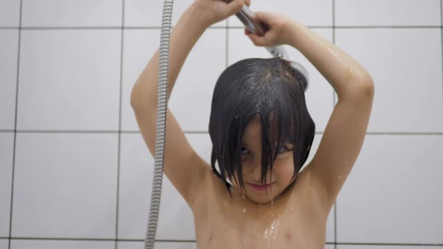 boy child 5 years old brunette with long hair washes in the bathroom and sings in the shower with white tiles in a square