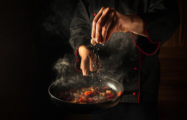 Cooking fresh vegetables. The chef adds salt to a steaming hot pan. Grande cuisine idea for a hotel with advertising space