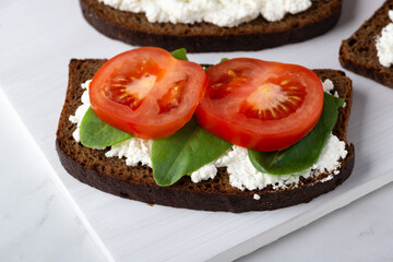 Slice of rye bread with cottage cheese and tomatoes on a wooden cutting board on a white background