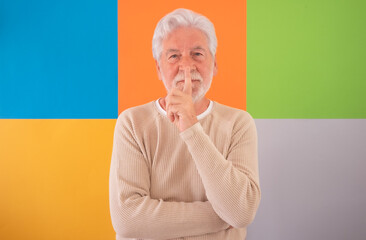 Shut up. Silence please. Adult handsome senior man looking at camera standing over colorful...