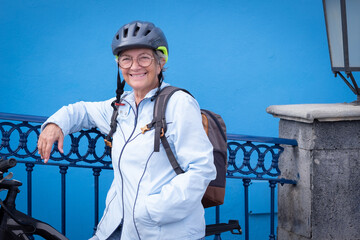 Joyful smiling mature caucasian woman wearing cyclist helmet looking at camera. Senior attractive happy woman resting close to her bicycle enjoying healthy and freedom lifestyle