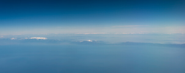 Fototapeta premium view from the airplane window to mountains clouds and blue sky