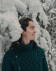 A young guy in a green sweater walks through a snowy forest