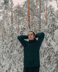 A young guy in a green sweater walks through a snowy forest