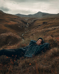 A young guy in a hat lies on the grass in the mountains