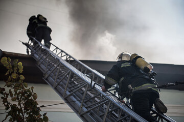 Firefighters on ladders in oxygen masks extinguish the fire in an old house in the middle of the...