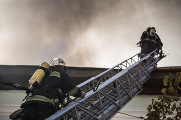 Firefighters on ladders in oxygen masks extinguish the fire in an old house in the middle of the...