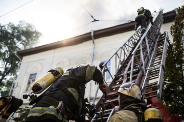 Firefighters on ladders in oxygen masks extinguish the fire in an old house in the middle of the...
