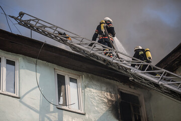 Firefighters on ladders in oxygen masks extinguish the fire in an old house in the middle of the...