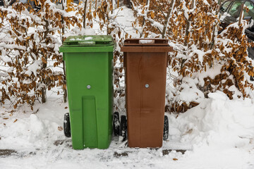 Close up view of two snow-covered waste sorting bins in private garden area on frosty winter day. Sweden.