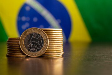 stack of Brazilian coins with a real highlighted and the Brazilian flag in the background....