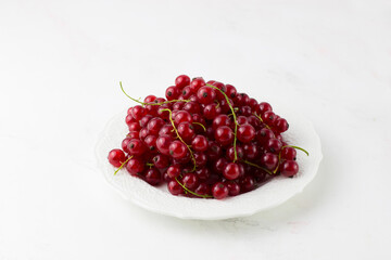 Red currants on a white plate on a white background. Useful berry