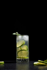 Un vaso de refrescante cóctel de desintoxicación de jugo de lima con rodajas de lima y hielo sobre fondo negro	