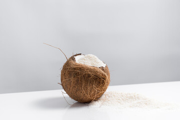 Coco abierto con hojuelas de coco ralladas que se derraman sobre una mesa blanca