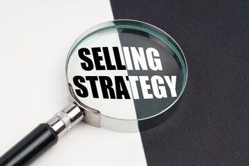 On the surface, which is half black and white, lies a magnifying glass inside which is written - SELLING STRATEGY