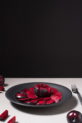 Rodajas de ciruelas negras y ciruelas enteras en un plato negro sobre una mesa gris	