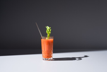 Vaso de jugo de zanahoria con hoja de apio servido con una paja sobre fondo gris