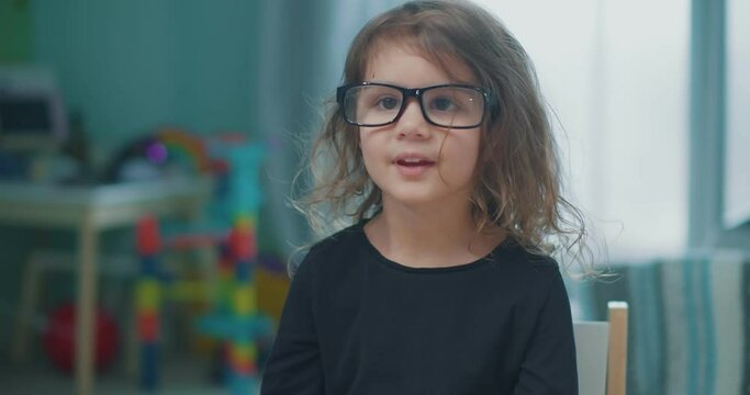 Cute toddler girl wearing silly adult oversize reading glasses. 4K footage.