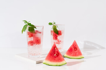 Dos vasos de zumo de sandía con hojas verdes trozos de sandia y hielo sobre fondo claro	