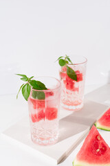 Dos vasos de zumo de sandía con hojas verdes trozos de sandia y hielo sobre fondo claro	