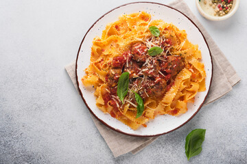 Tagliatelle pasta with meatballs in tomato sauce and thyme in sauce on light grey slate, stone or concrete background. Traditional Italian dish and cuisine. Top view with copy space.