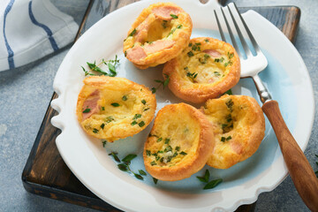 Egg muffins with green onions, bacon, cheese and tomatoes on white plate on light background. Healthy high protein and low carb breakfast, ready to eat.