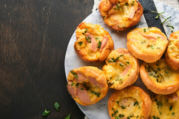 Delicious egg muffins with green onions, bacon, cheese and tomatoes on wooden board on old wooden rustic background. Healthy high protein and low carb breakfast. Homemade food.